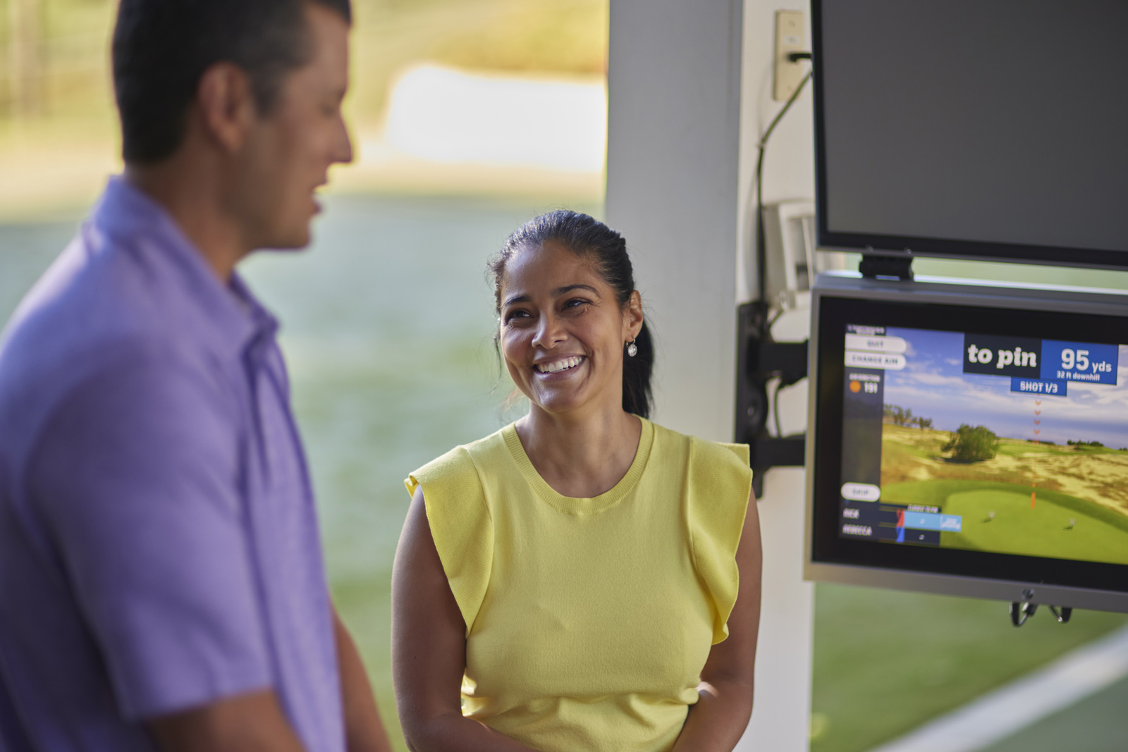 A man and a woman are smiling and talking. In the background, there is a screen showing the results of their last swings.
