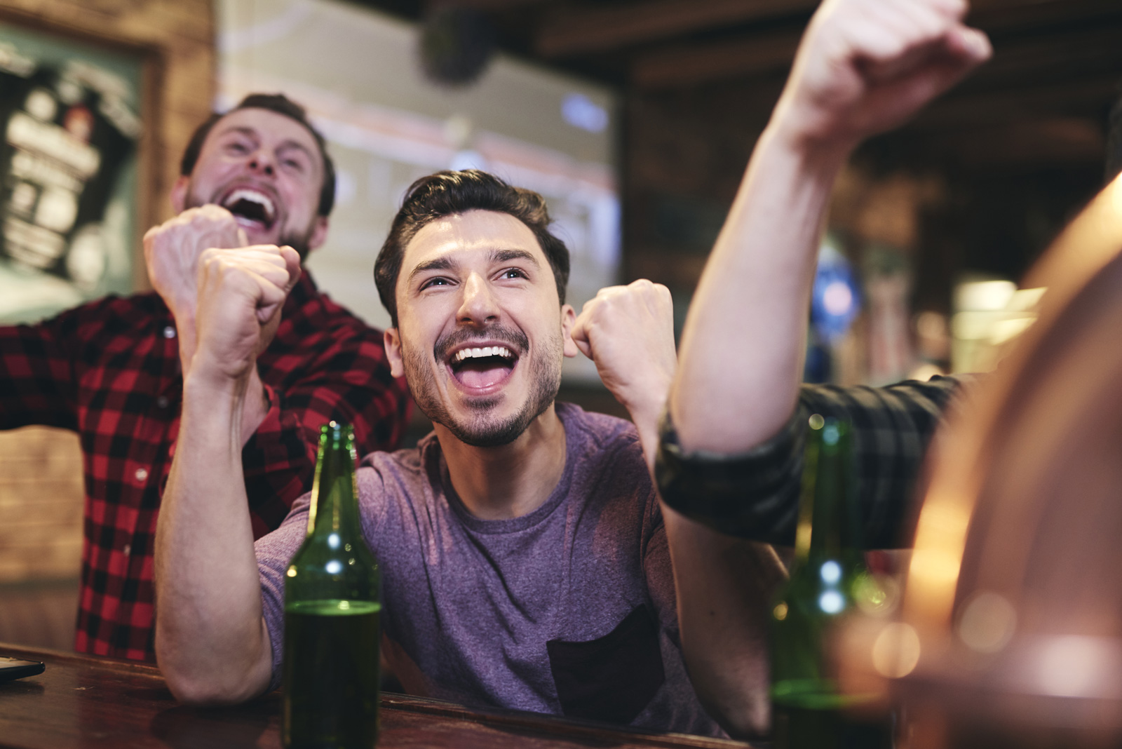 Two men are leaning against a bar watching sports on the televisions and celebrating a victory in a lively atmosphere.