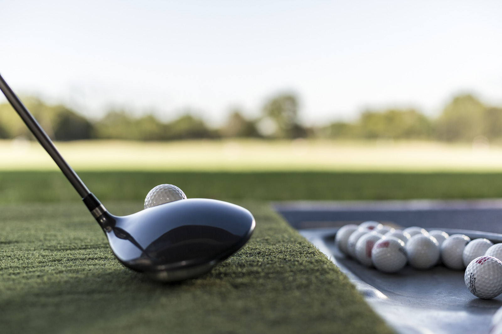 Gros plan sur un bâton de golf placé devant une balle sur une surface de gazon synthétique qui s’ouvre sur un terrain extérieur.