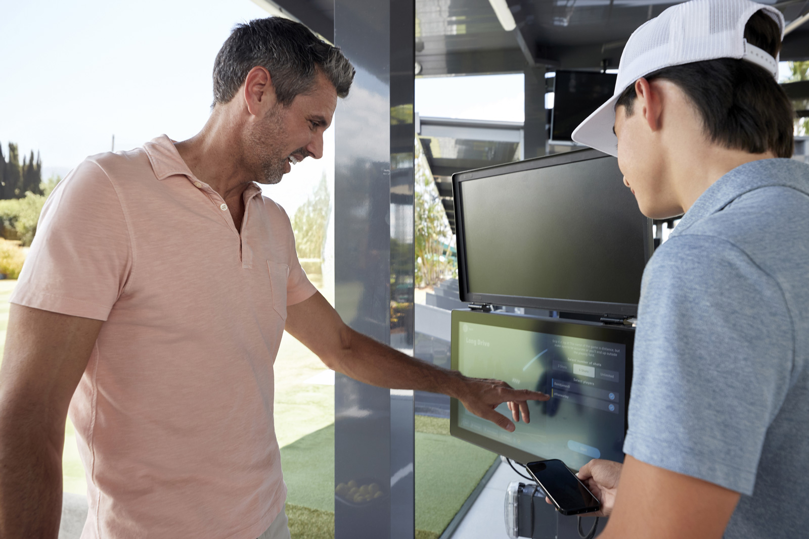 Two golfers standing in front of a screen, smiling and filling out their player profiles.