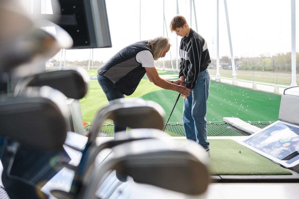 Young golfer receiving advice from a coach on best posture before swinging.